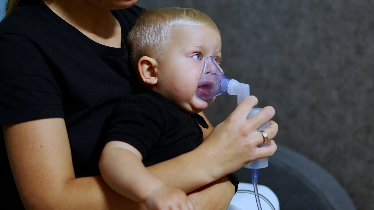 Malý chlapec sedí na gauči a inhaluje pomocí inhalátoru. Terapeutická inhalace pro děti. Inhalační maska pro děti.