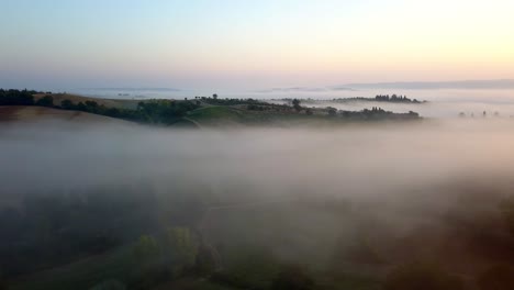 farm fields in toscany italy on a foggy morning during sunrise, aerial slow lowering shot