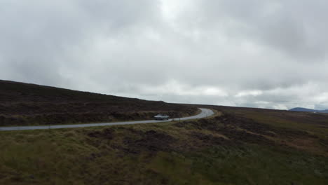 Tracking-of-vintage-sports-car-passing-on-road-through-large-moorlands-in-countryside.-Overcast-sky.-Ireland