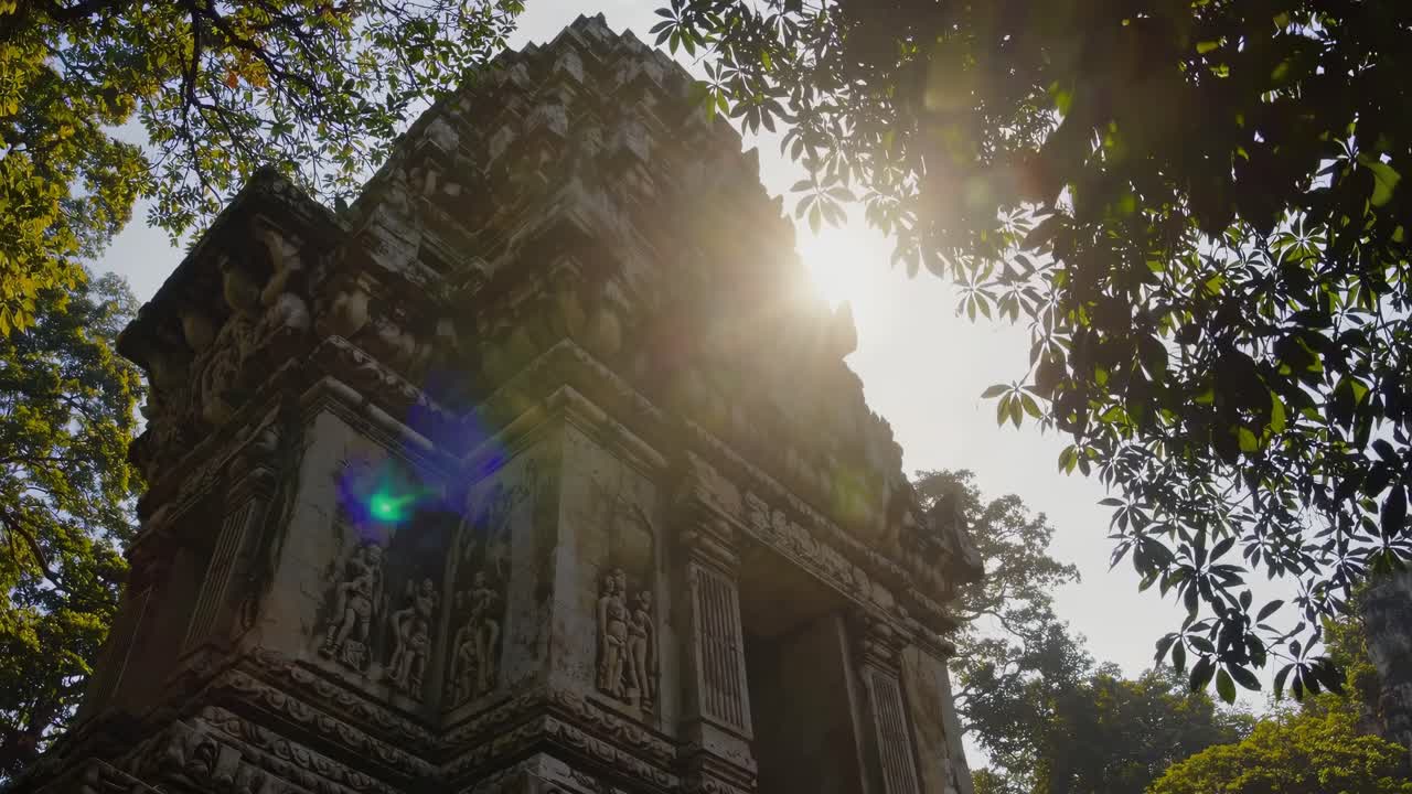 Low-angle video shot of an ancient temple tower framed by lush green leaves, capturing sunlight