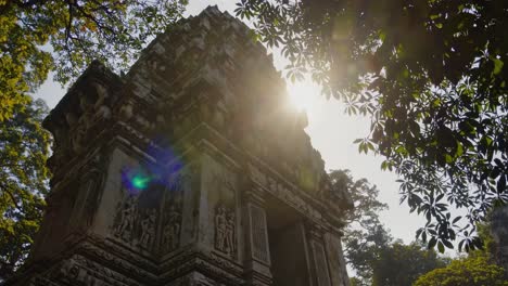 low-angle video shot of an ancient temple tower framed by lush green leaves, capturing sunlight