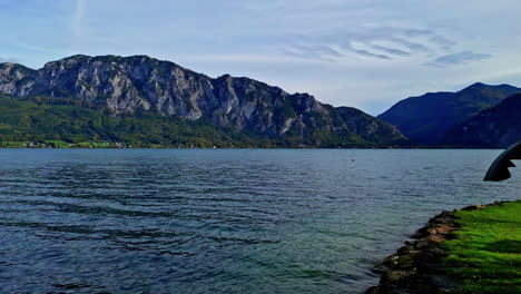 a tracking shot of a lake and a green landscape with mountains and a calm weather