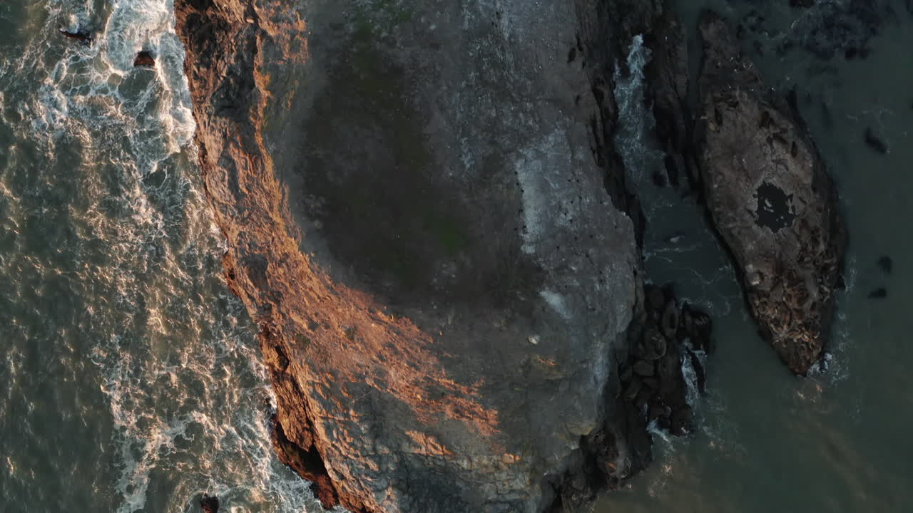 Birds Eye Aerial Shot of Waves Crashing against a Rocky Outcrop at Sunset