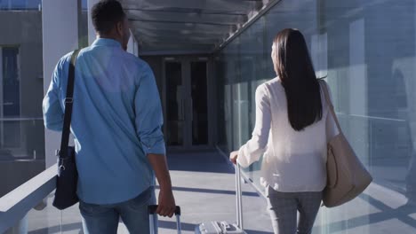 video of back of diverse man and woman walking with suitcases