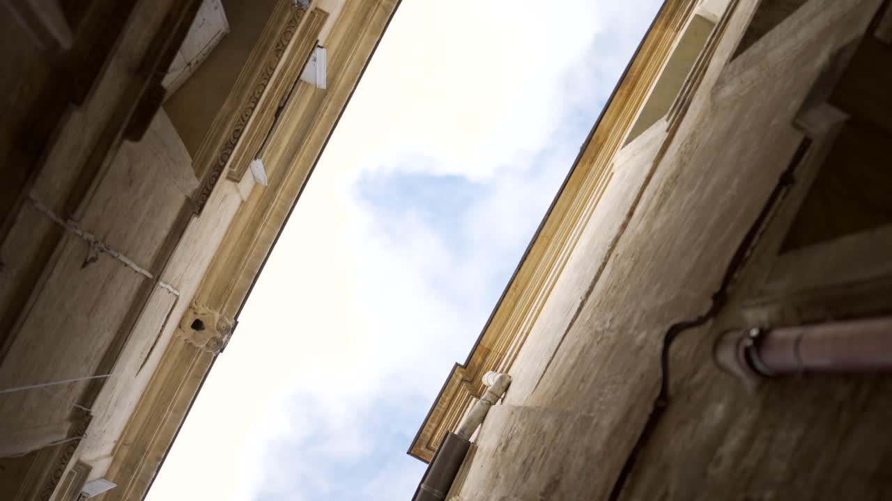 toma de pov mirando hacia arriba entre dos viejos edificios de piedra en una calle de un pueblo del sur de francia, en un hermoso día con cielo azul, giro y efecto de vértigo