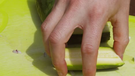 male person hand slicing organic courgette zucchini vegetable in half in sunlight outside - 4k slow motion