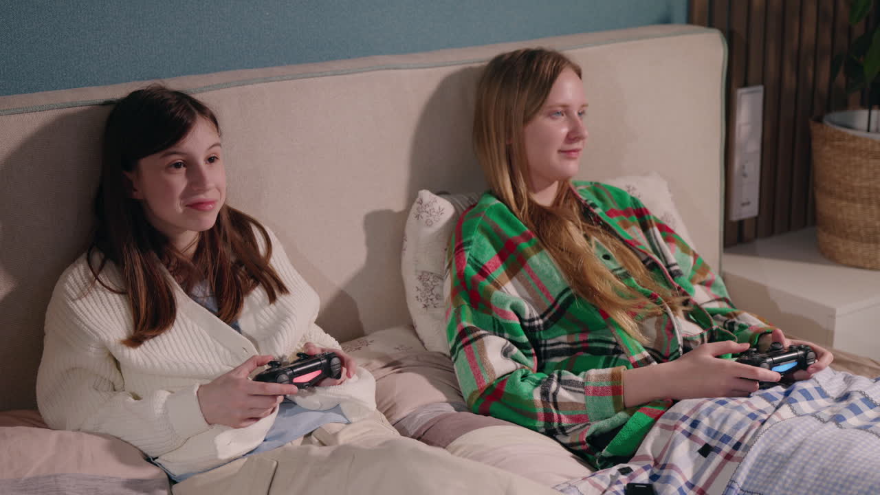 Teenage girls playing video games in bed