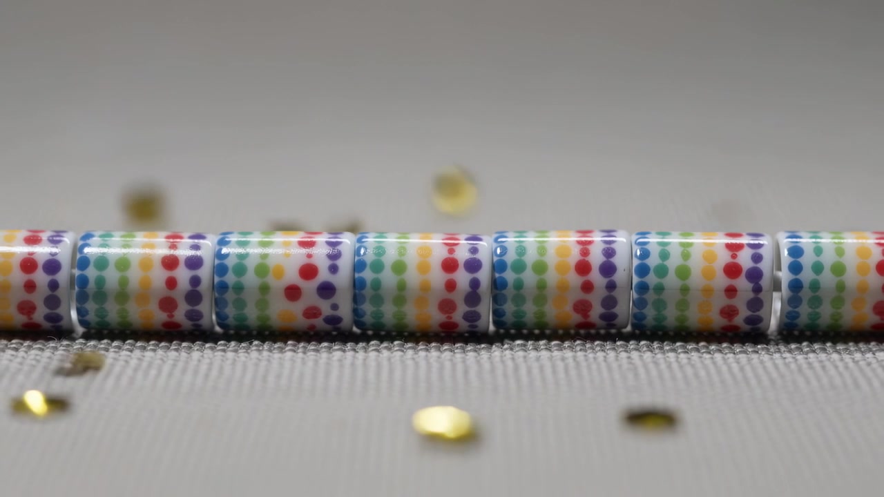 Vallende pailletten zweven van bovenaf over een getextureerde mat, langs een gecentreerde rij regenboogstipparels