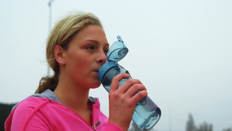 front view of young caucasian female athlete drinking water at sports venue 4k