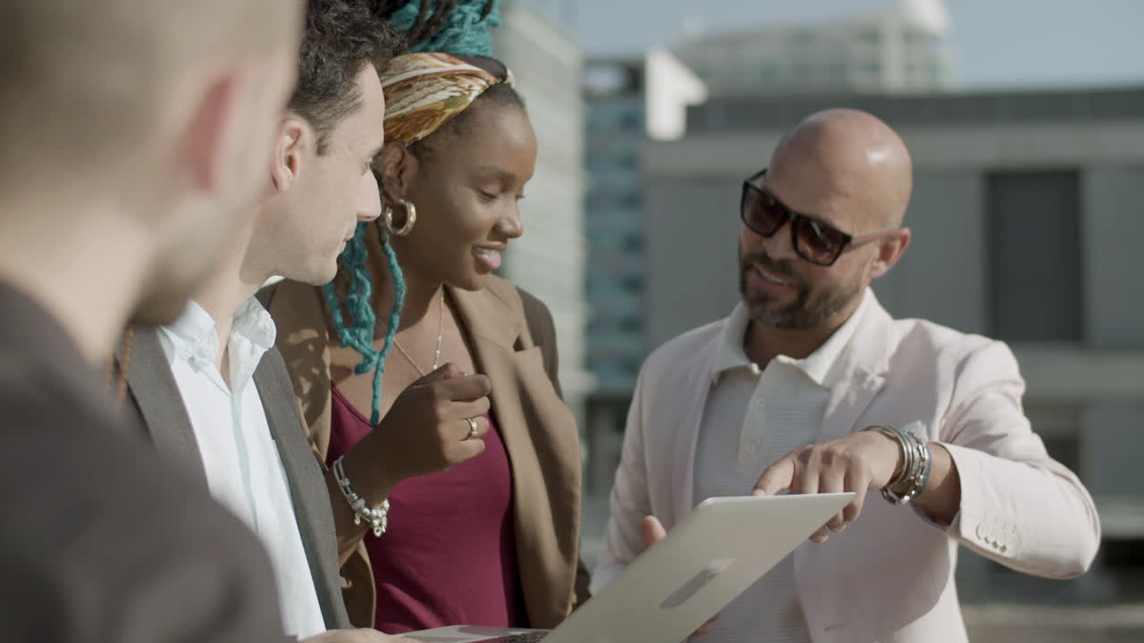 compañeros de trabajo felices de pie en la azotea y mirando la computadora portátil
