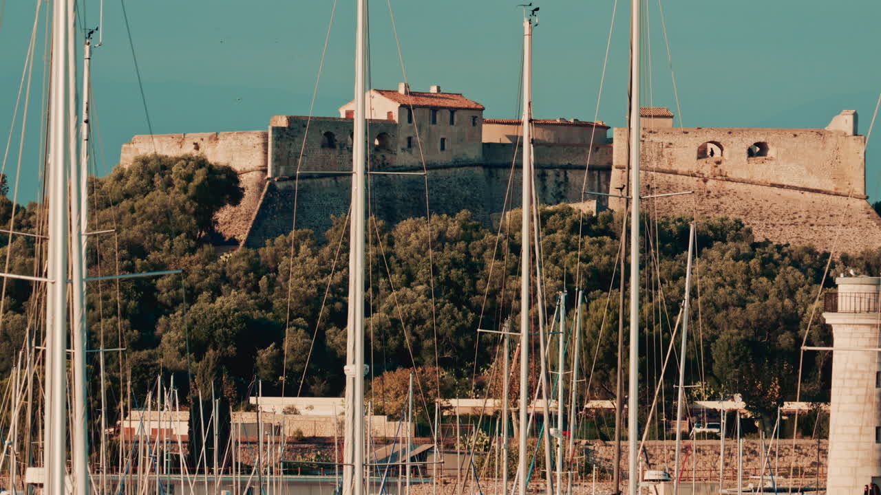 A historic stone fortress stands on a hill behind a dense marina full of sailboat masts