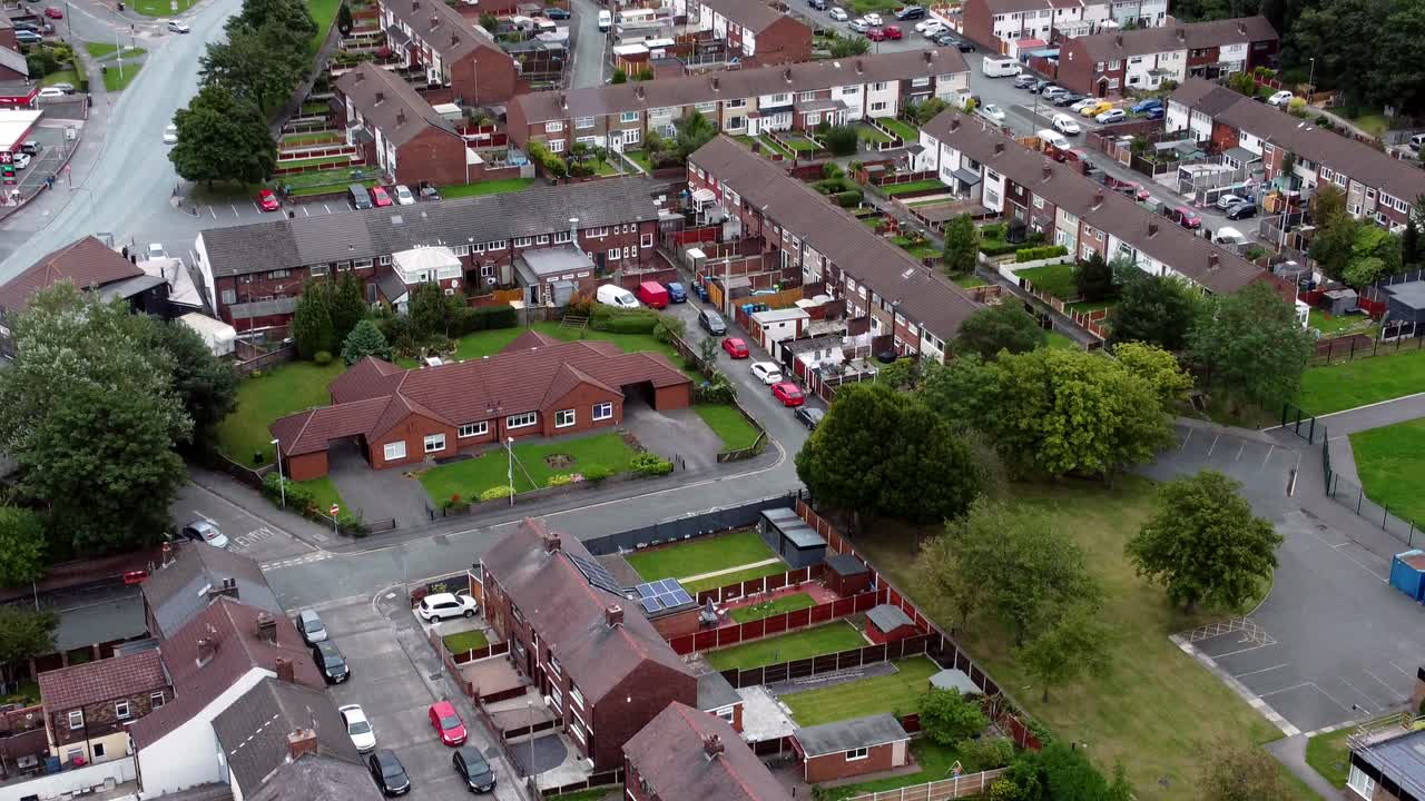 Aerial view above British neighbourhood small town residential suburban property gardens and town streets slow tilt up