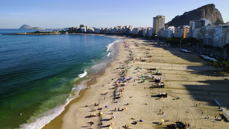 Drone-rising-over-people-on-the-Copacabana-Beach,-golden-hour-in-Rio-de-Janeiro