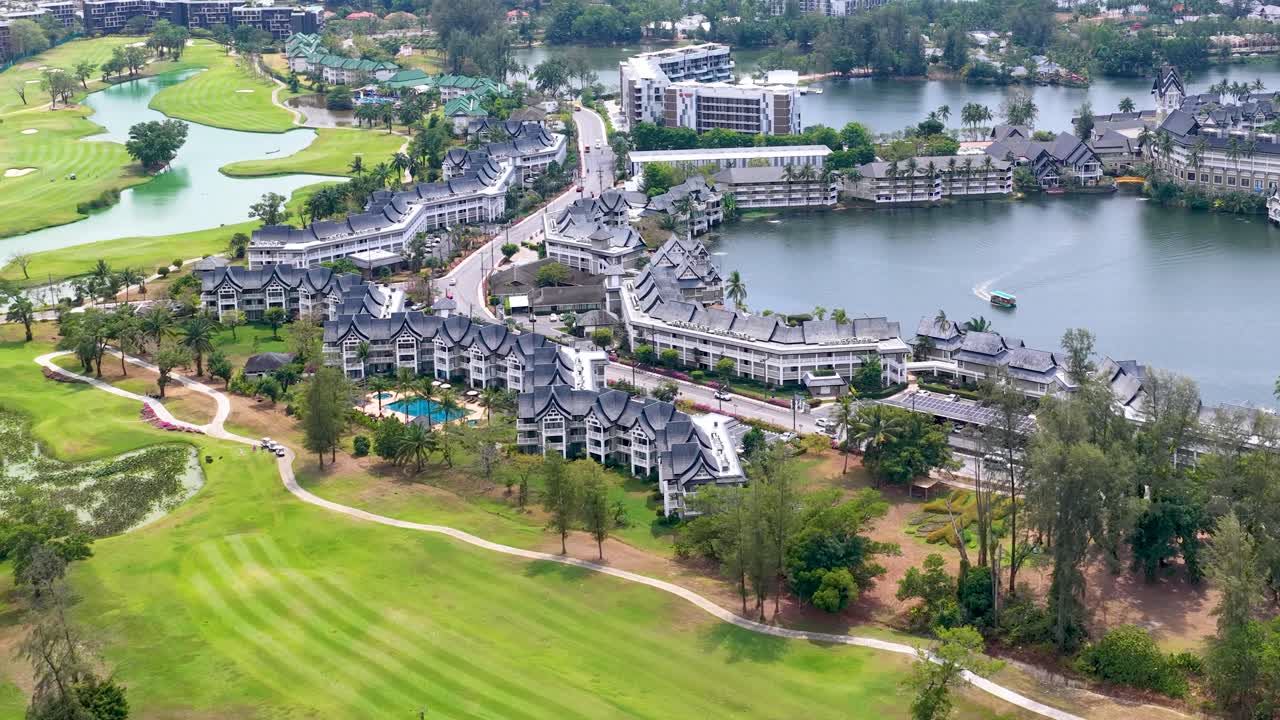 Cảnh quay bằng drone góc cao lia máy qua một sân golf nhiệt đới và khu căn hộ ven hồ sang trọng.