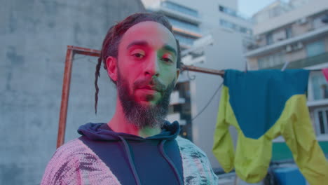 portrait of bearded man with dreadlocks in neon light on urban rooftop