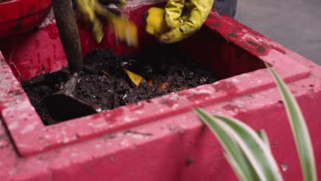 a person with yellow gloves adding kitchen scraps to a compost bin