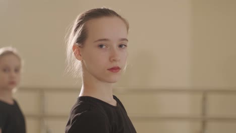 a group of young ballet students in black dancewear practicing positions in a spacious ballet studio with wooden flooring and wall-mounted barres. focused expressions and synchronized movements.