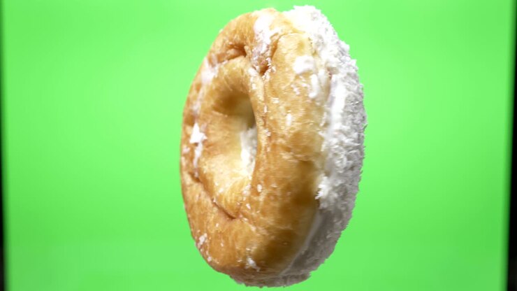 Shot of delicious white donut with coconut chips spinning around on green background.