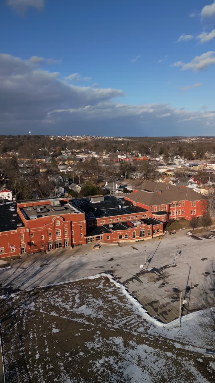 Aerial vertical establishing of suburban school surrounded by houses with cityscape in the distant background