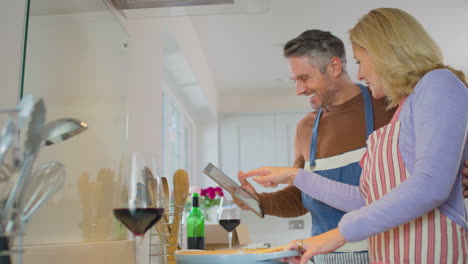 mature couple at home following recipe on digital tablet in kitchen as they prepare meal together - shot in slow motion