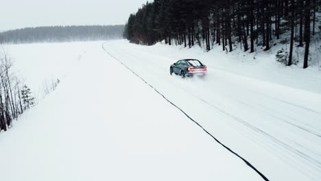 an electric car is driving on a snow-covered road in the arctic circle during a snowfall, followed by a drone