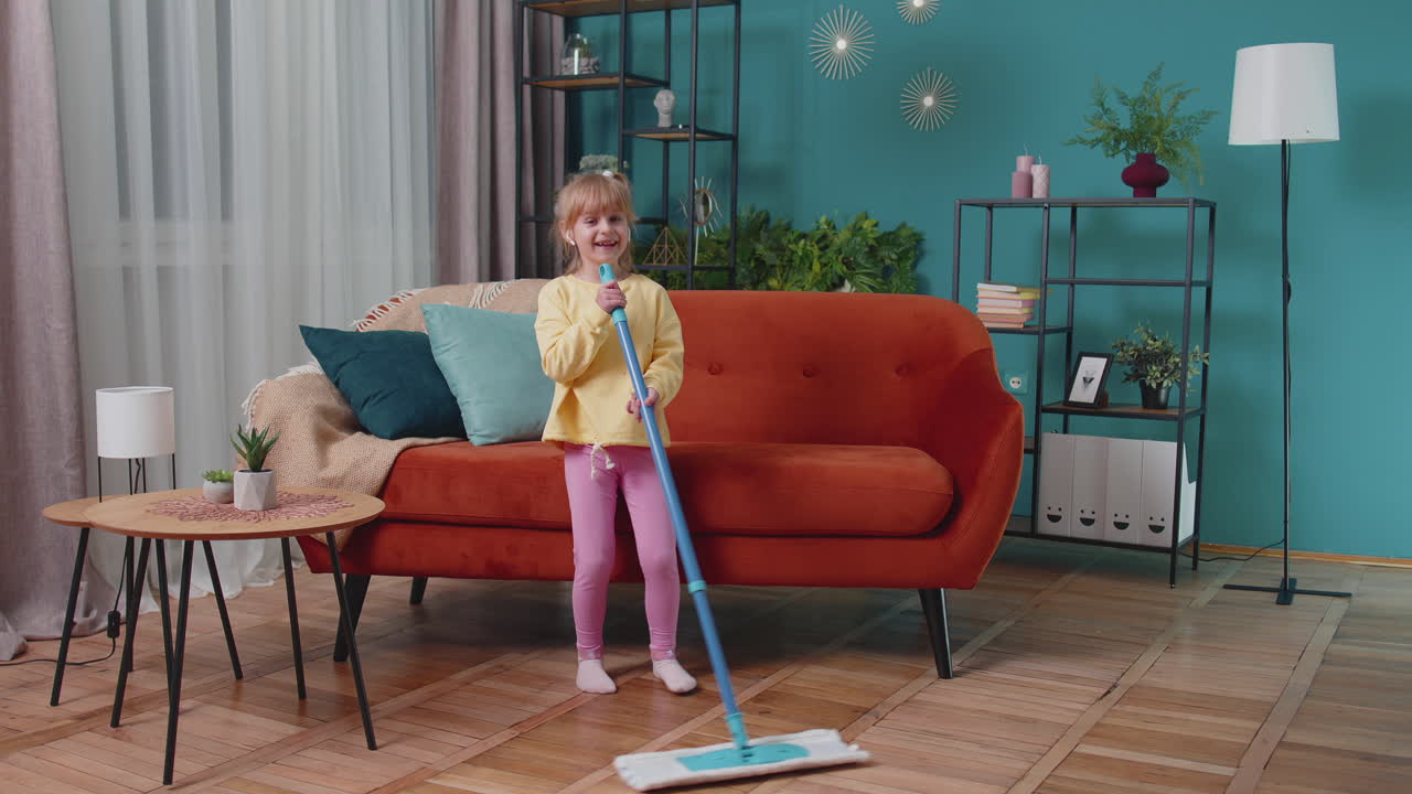 Child girl kid washes floors with a mop in domestic living room dancing, singing in positive mood