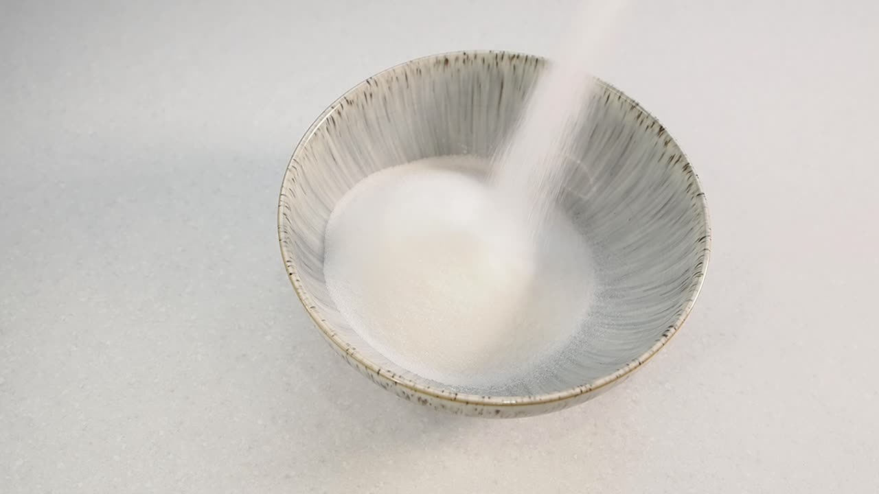 Zucchero bianco versato in una ciotola di ceramica grigia.