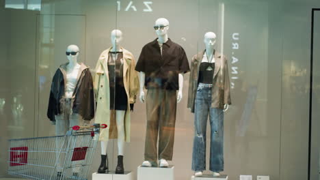 view of male and female mannequins dressed in stylish outfits displayed in a mall. a shopping trolley is visible in the background, adding a retail context