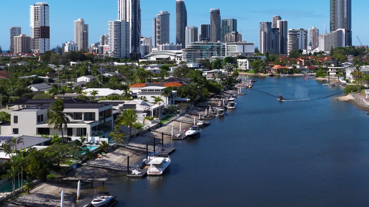 Drone footage captures a serene canal with boats and the Gold Coast skyline under clear blue skies