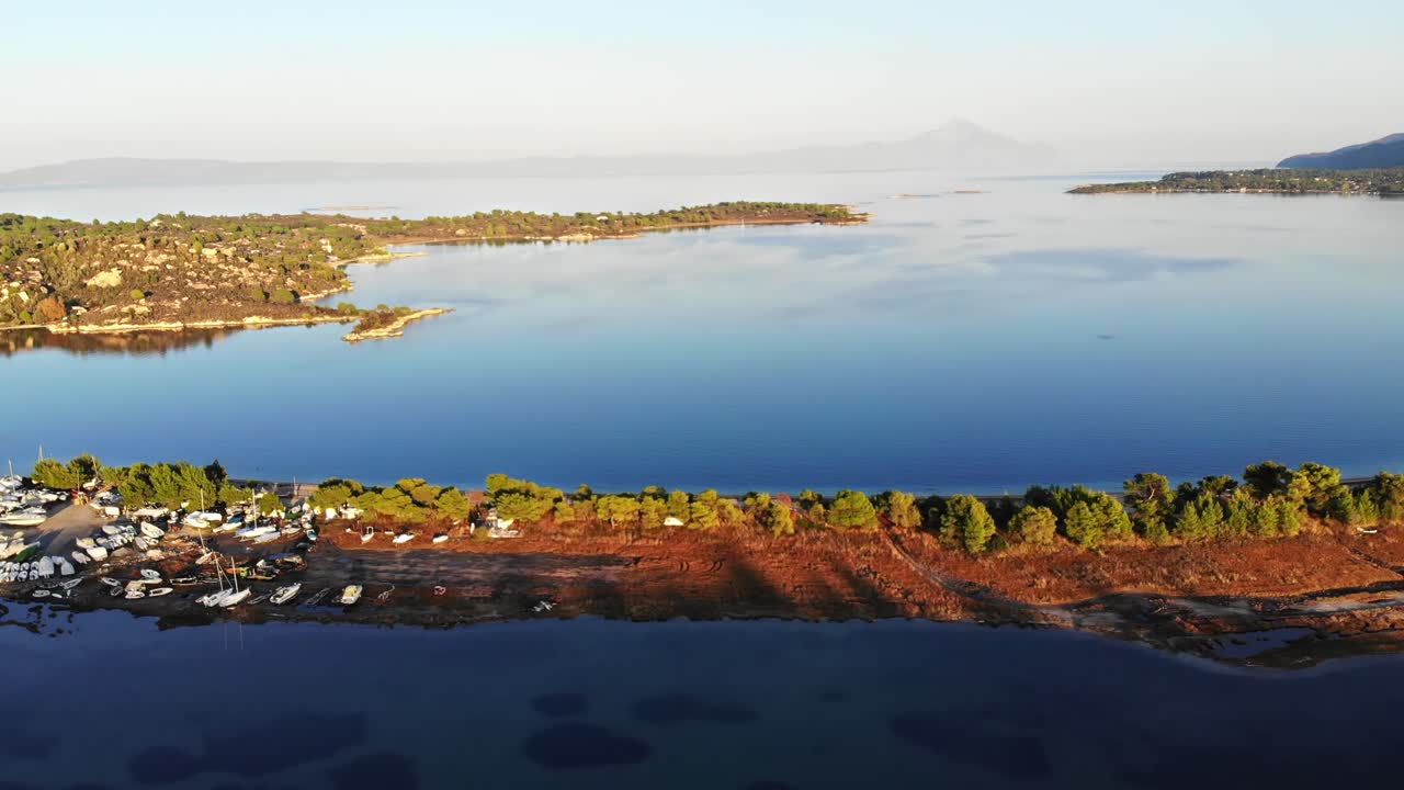 Vista aérea de drone de uma ilha no Mar Egeu com vários iates e barcos atracados, pedras, vegetação ao redor, pôr do sol, Grécia