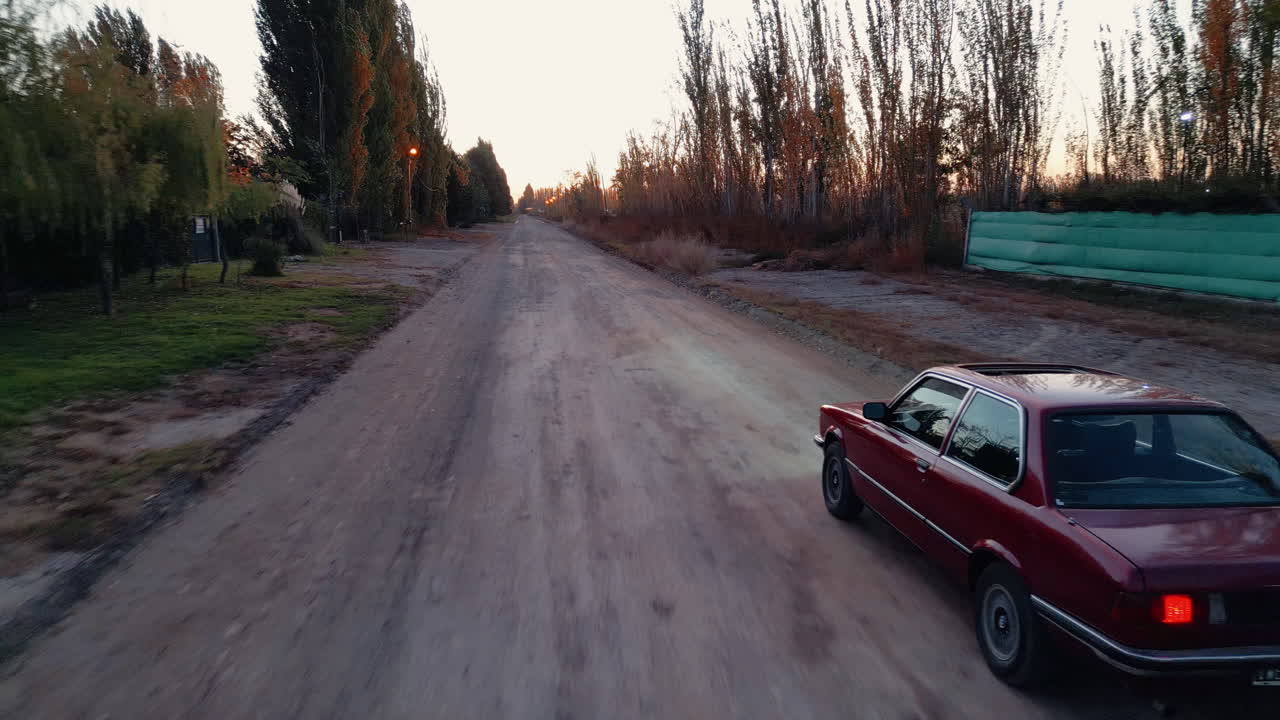 Rotes Auto fährt bei Sonnenuntergang auf einem ländlichen Feldweg davon.