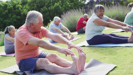 diverse group of happy male and female seniors exercising in garden, touching toes, slow motion