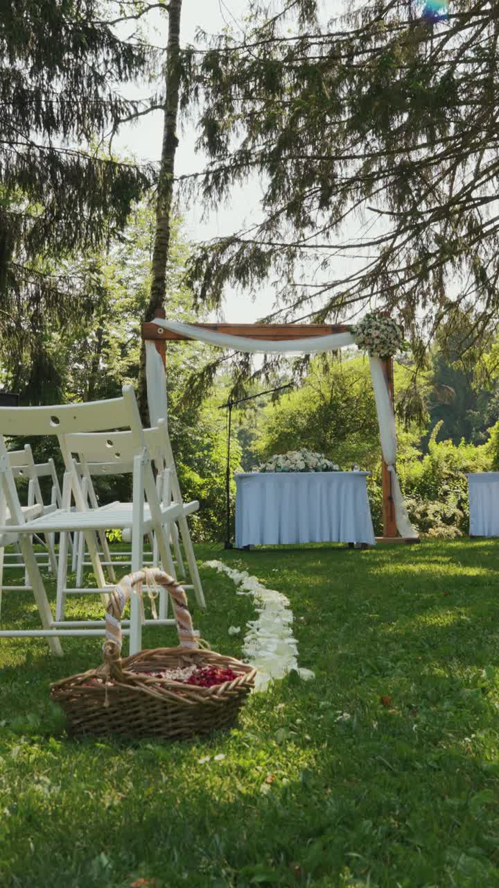 Vertical: wedding ceremony with an arch and white chairs during the day in the forest, medium shot