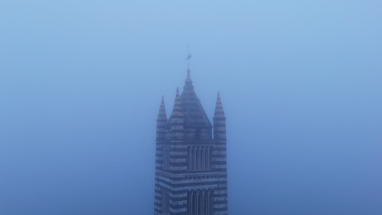 la torre gótica de la catedral de siena emerge a través de la densa niebla en la toscana, creando una escena misteriosa.