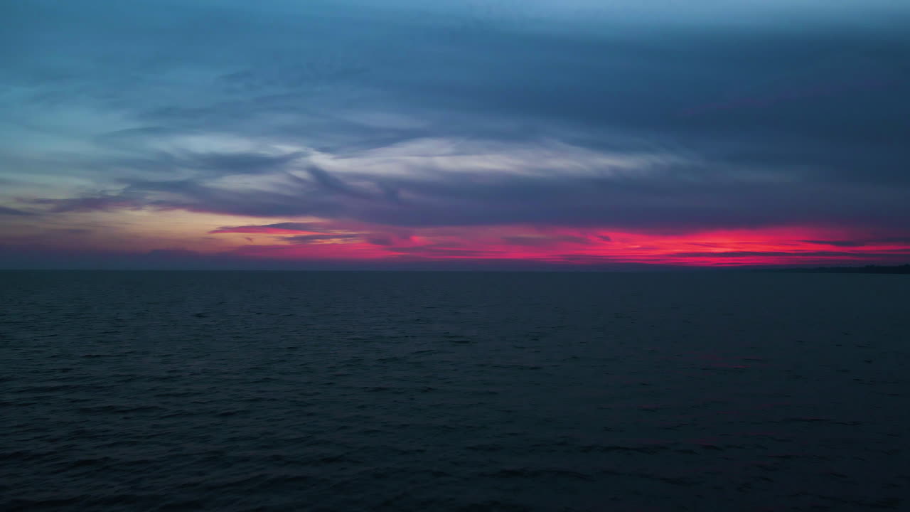 Aerial dolly out to sunset's last light of pink red hues above water