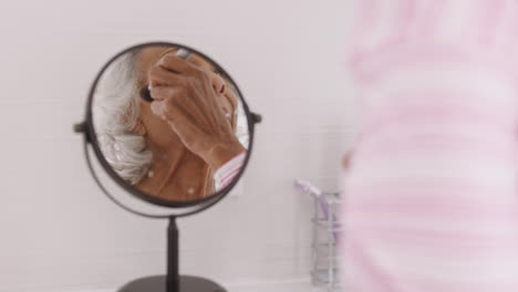 mujer mayor mirando el reflejo en el espejo del baño poniendo maquillaje