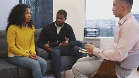 unhappy couple sitting on couch meeting with male counsellor in office