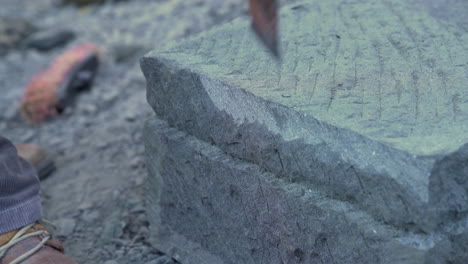 closeup shot of a stone craftsman shaping the edge of a stone pillar with a handheld pick, using local cancagua stone in the city of ancud, chiloe island