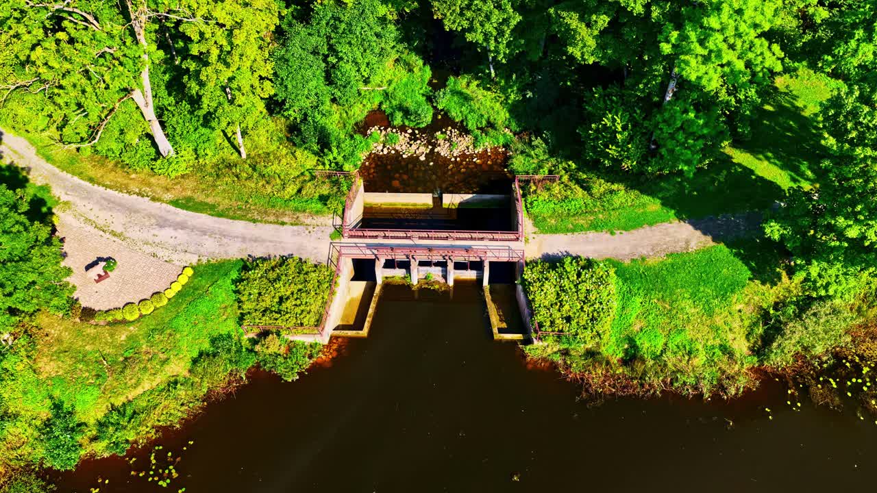 Dam spillway on a body of water surrounded by trees forest path, aerial drone