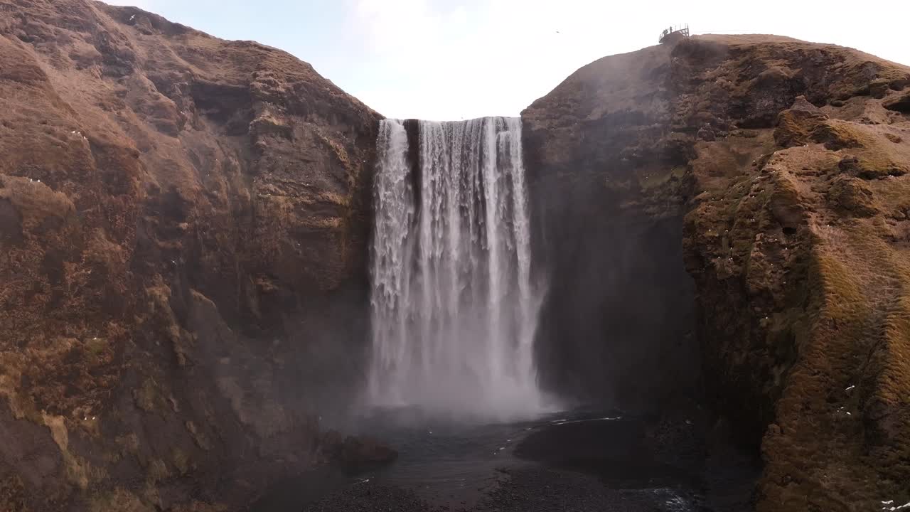 Majestic frontal view of Skógafoss waterfall in southern Iceland, where the Skógá River cascades over ancient sea cliffs near Eyjafjallajökull volcano, framed by mist and rocky terrain.