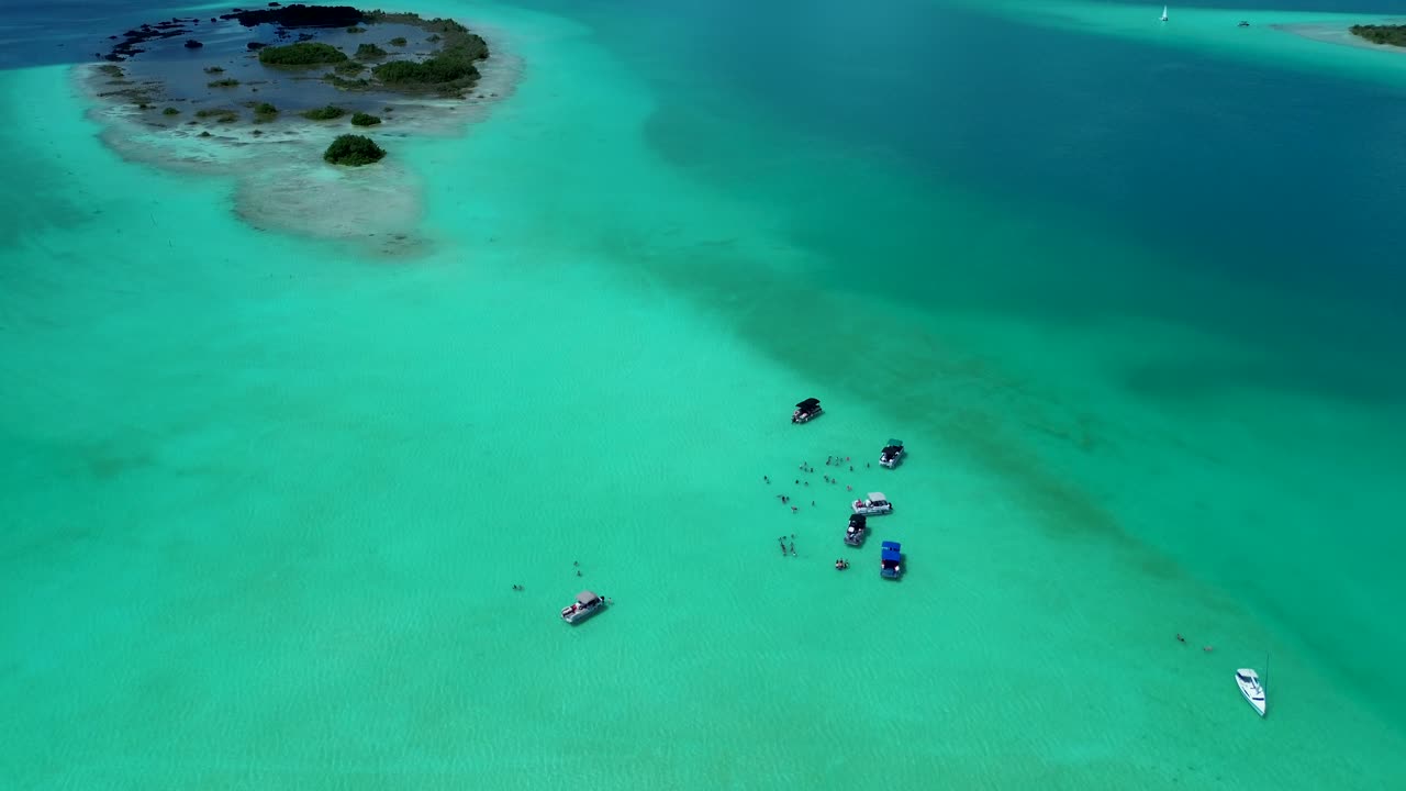 Drone aerial landscape of people swimming with tour boats docked on sandbar lagoon lake inlet island snorkelling spot Bacalar town village Mexico travel holidays tourism