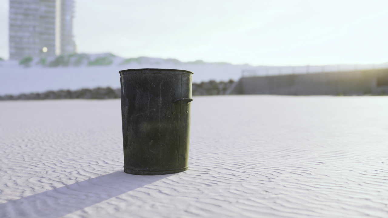 Trash bin stands alone on a clean sandy beach during sunset in a coastal city