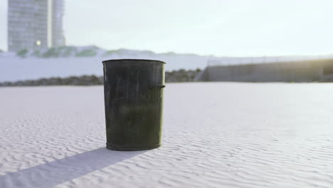 trash bin stands alone on a clean sandy beach during sunset in a coastal city