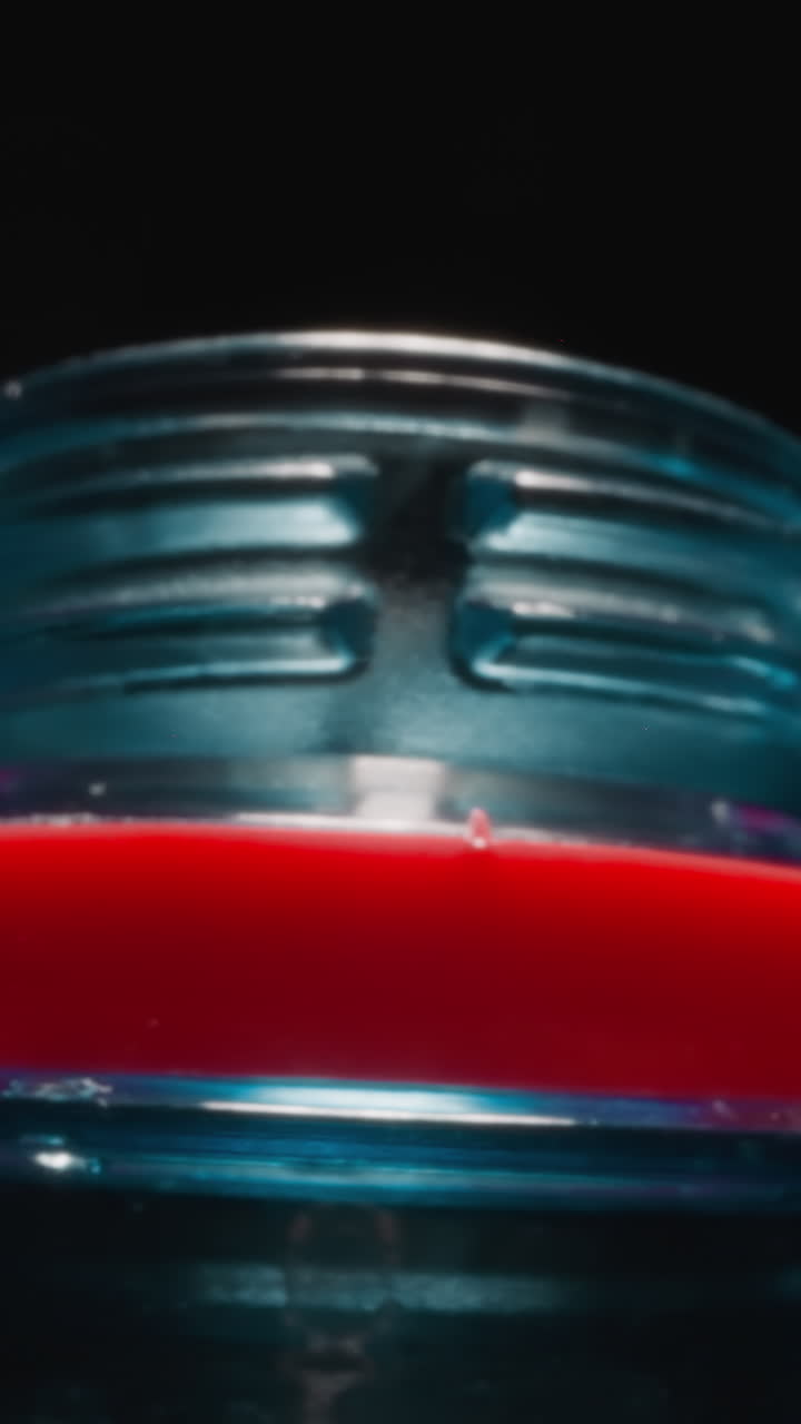 Neck of open plastic bottle with red ring for drinking water at bright studio light. Transparent container used for liquid on black background macro