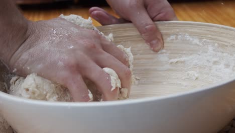 El-Chef-Moldea-La-Masa-De-Pizza-En-Un-Plato-Hondo,-Sobre-Una-Mesa-De-Madera