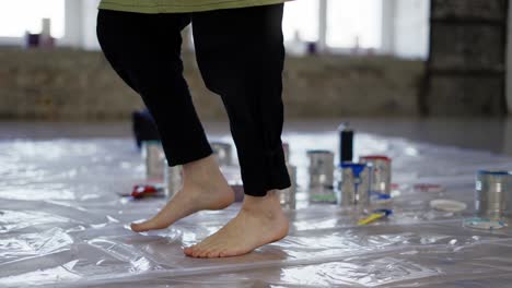 View-of-paint-cans-on-floor,-female-feet-she-dances-on-oilcloth