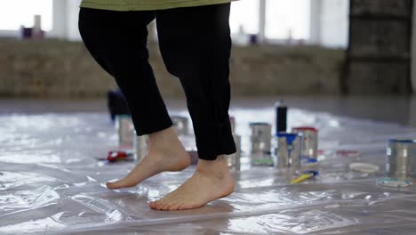 vista de latas de pintura en el suelo, pies femeninos ella baila en el paño de aceite