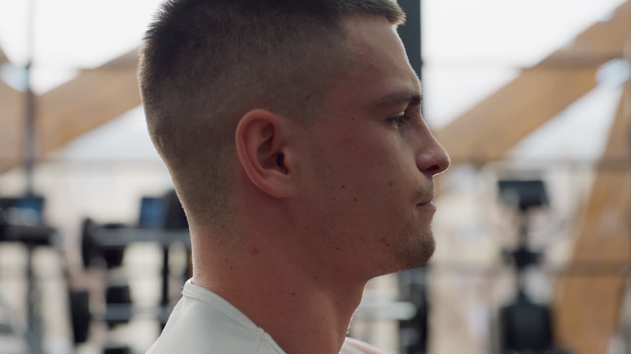Side view profile of fitness fanatic executing chest press on weight machine with face contorted in intense effort, sweat beading on skin as light illuminates focused muscles flexing under tension