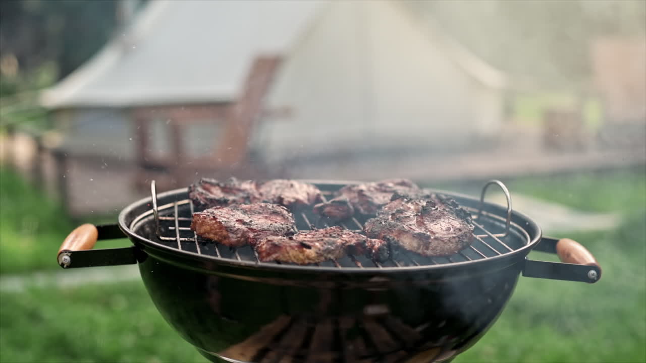 Young man frying meat on the grill. Greenery around. Glamping. Slow motion