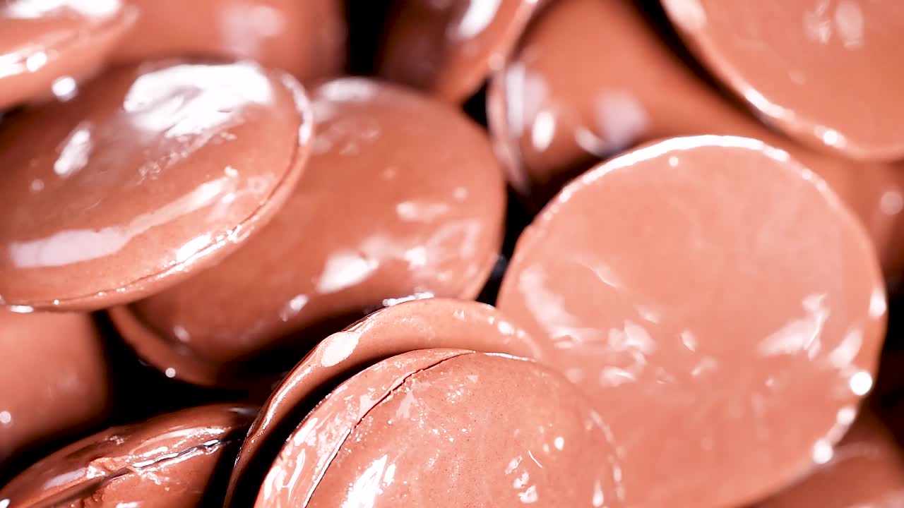 Close-up view of shiny chocolate discs being mixed with a spoon, highlighting their smooth texture.